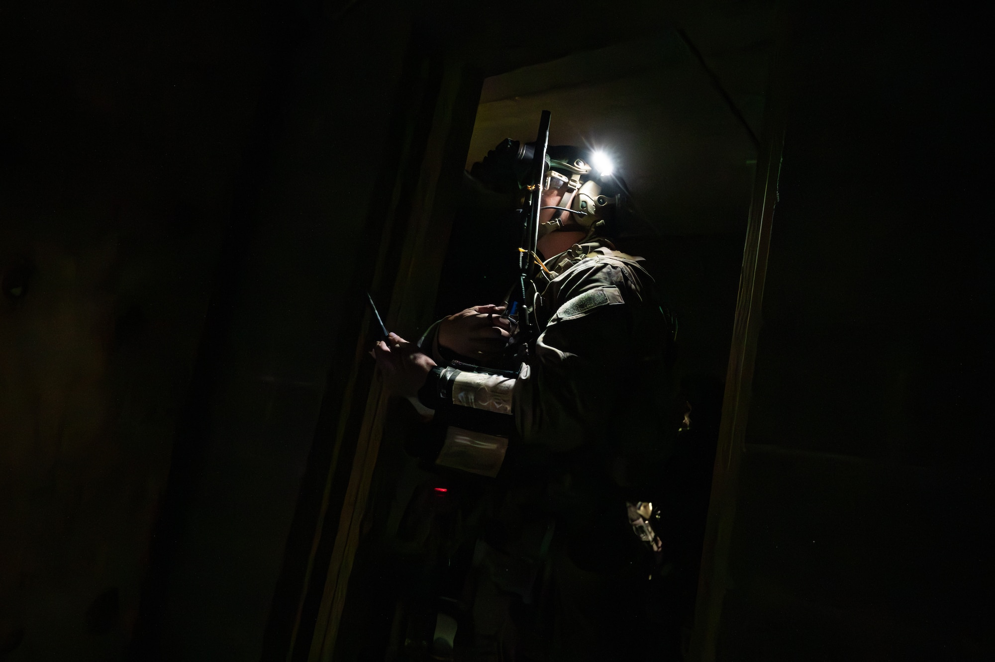 A U.S. Army Green Beret is illuminated by a headlight while speaking on a radio in a dark room.