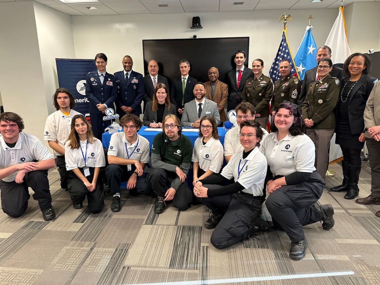 A large group of people, including uniformed service members and civilians, pose for a photo.