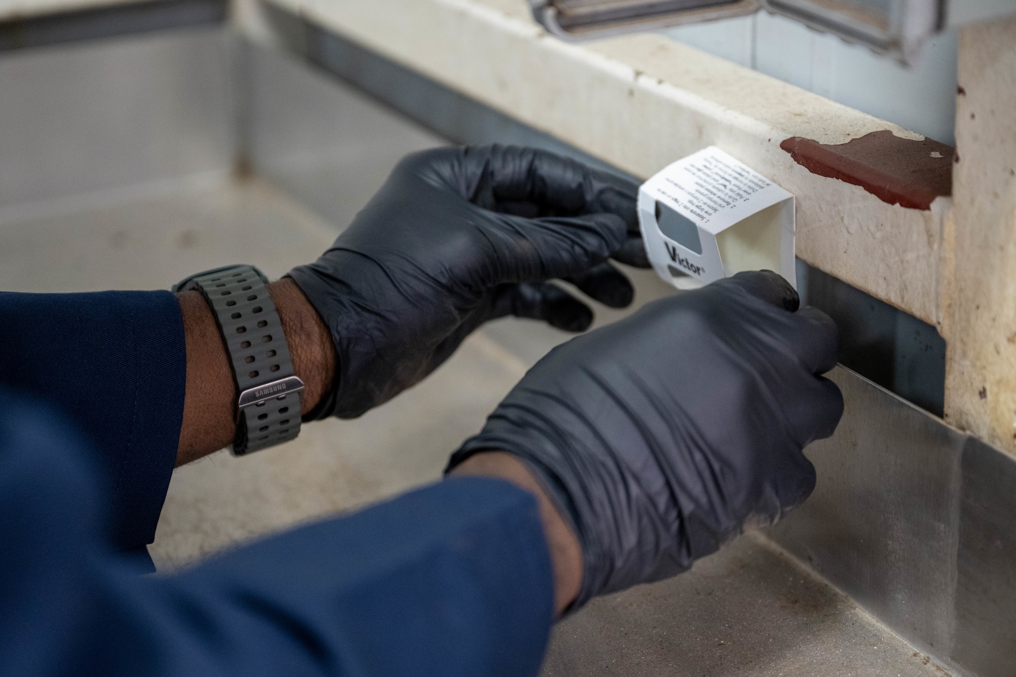 U.S. Air Force Airmen surveys a dining facility kitchen and sets a trap for roaming pests.