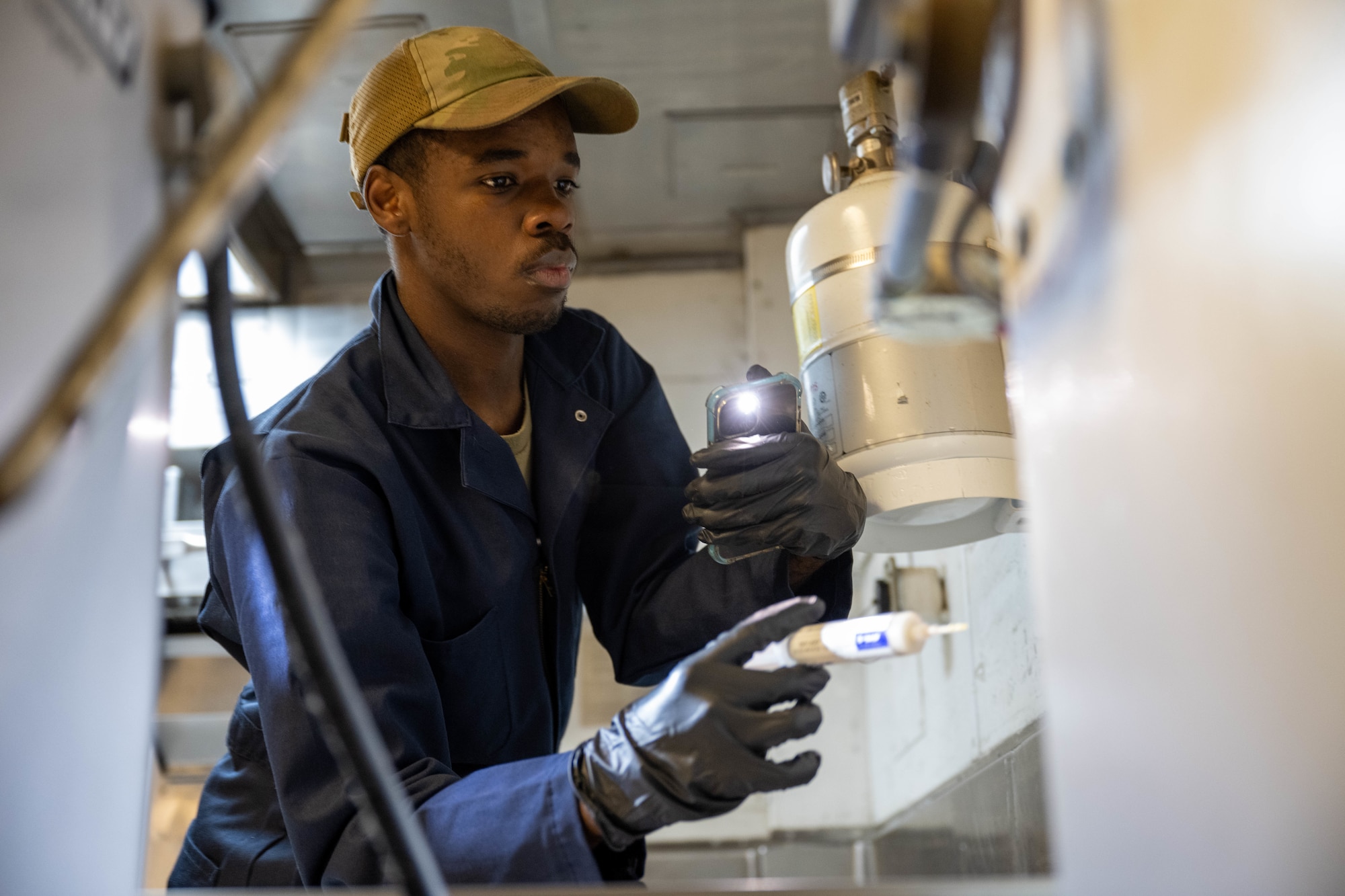 U.S. Air Force Airmen surveys a dining facility kitchen and applies a pesticide paste for roaming pests.