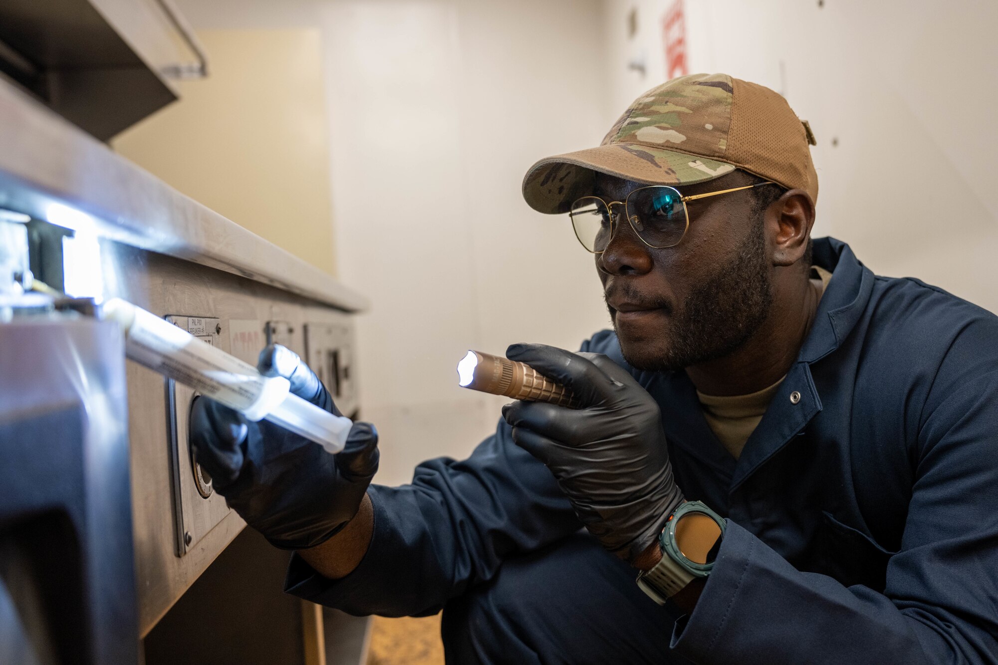U.S. Air Force Airmen surveys a dining facility kitchen and applies a pesticide paste for roaming pests.