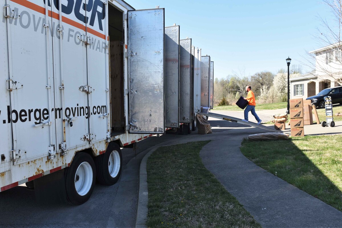 A man hoists a box while walking up a ramp into a truck trailer.