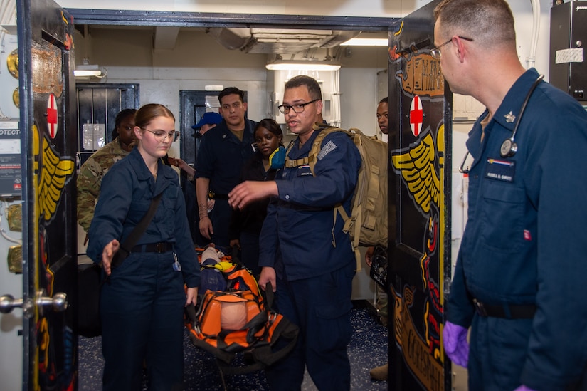 U.S. Army Sgt. Jaliah Rudolph, back left, from Montgomery, Alabama, assigned to 62nd Medical Brigade, stationed at Joint Base Lewis-McChord, assists Sailors in transporting a simulated casualty during a joint Tactical Combat Casualty Care training between Soldiers and Sailors in the main battle dressing station onboard Nimitz-class aircraft carrier USS Ronald Reagan (CVN 76), while underway in the U.S. 3rd Fleet area of operations, Dec. 5, 2024. Ronald Reagan provides a combat-ready force that protects and defends the United States, and supports alliances, partnerships and collective maritime interests in the Indo-Pacific region. (U.S. Navy photo by Mass Communication Specialist 2nd Class Eric Stanton)