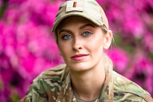woman in uniform poses in front of pink flowers