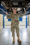 a man in uniform stands under a vehicle on a lift in a garage