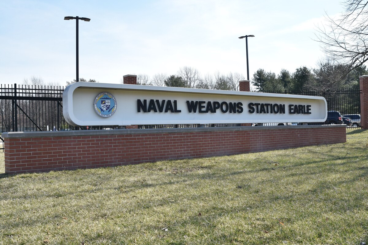 A large sign mounted on a brick wall reads "Naval Weapons Station Earle."