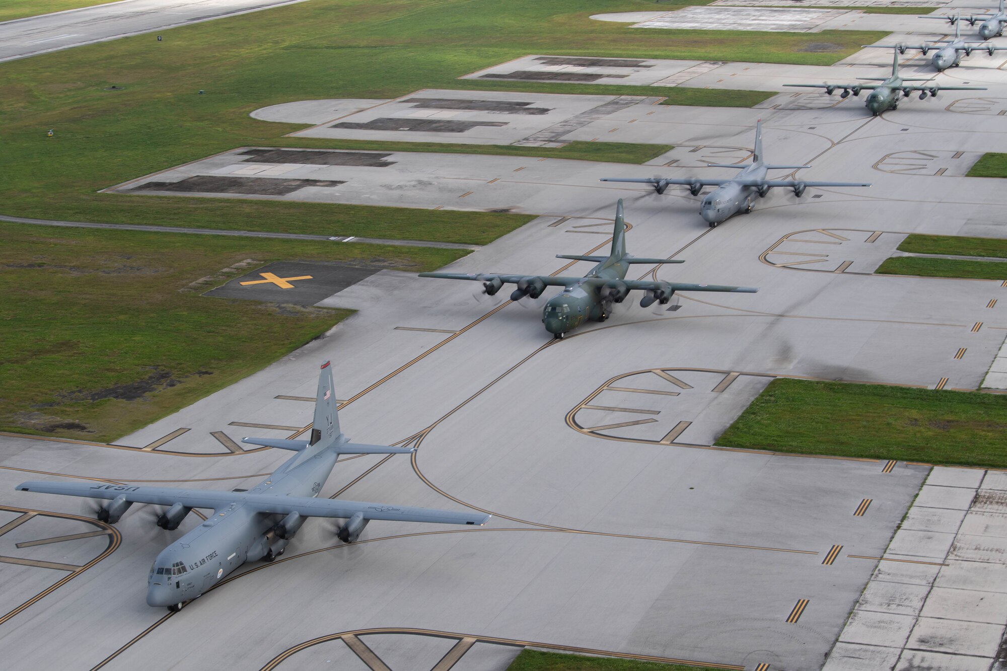 Six C-130 drive on a flight line.