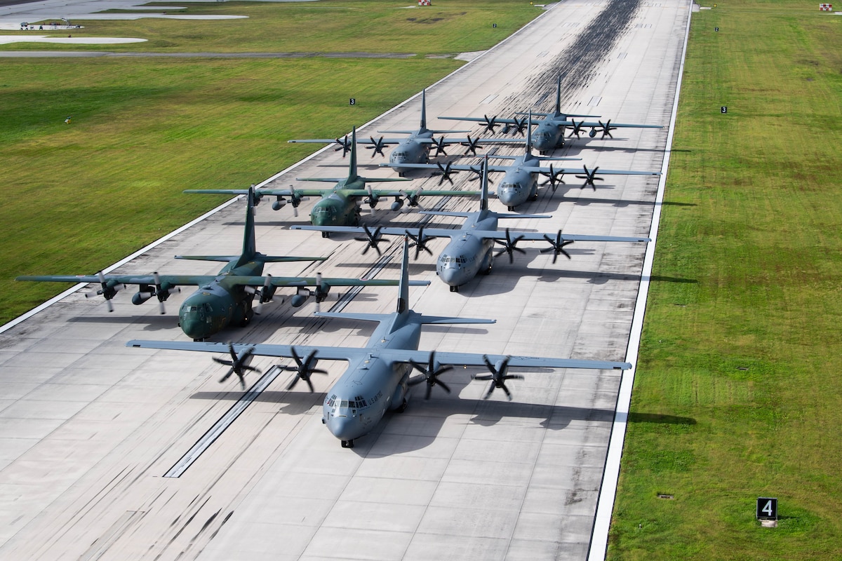 Seven planes sit on a runway in formation.