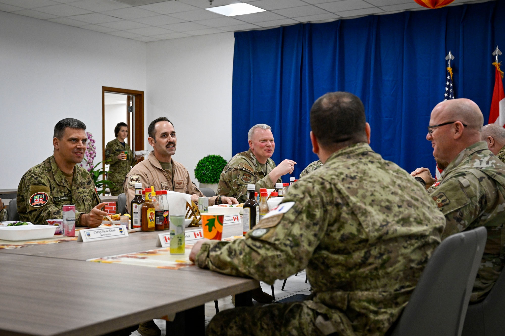 Canadian Armed Forces military members and U.S. Air Force military members talk while sitting at a table.