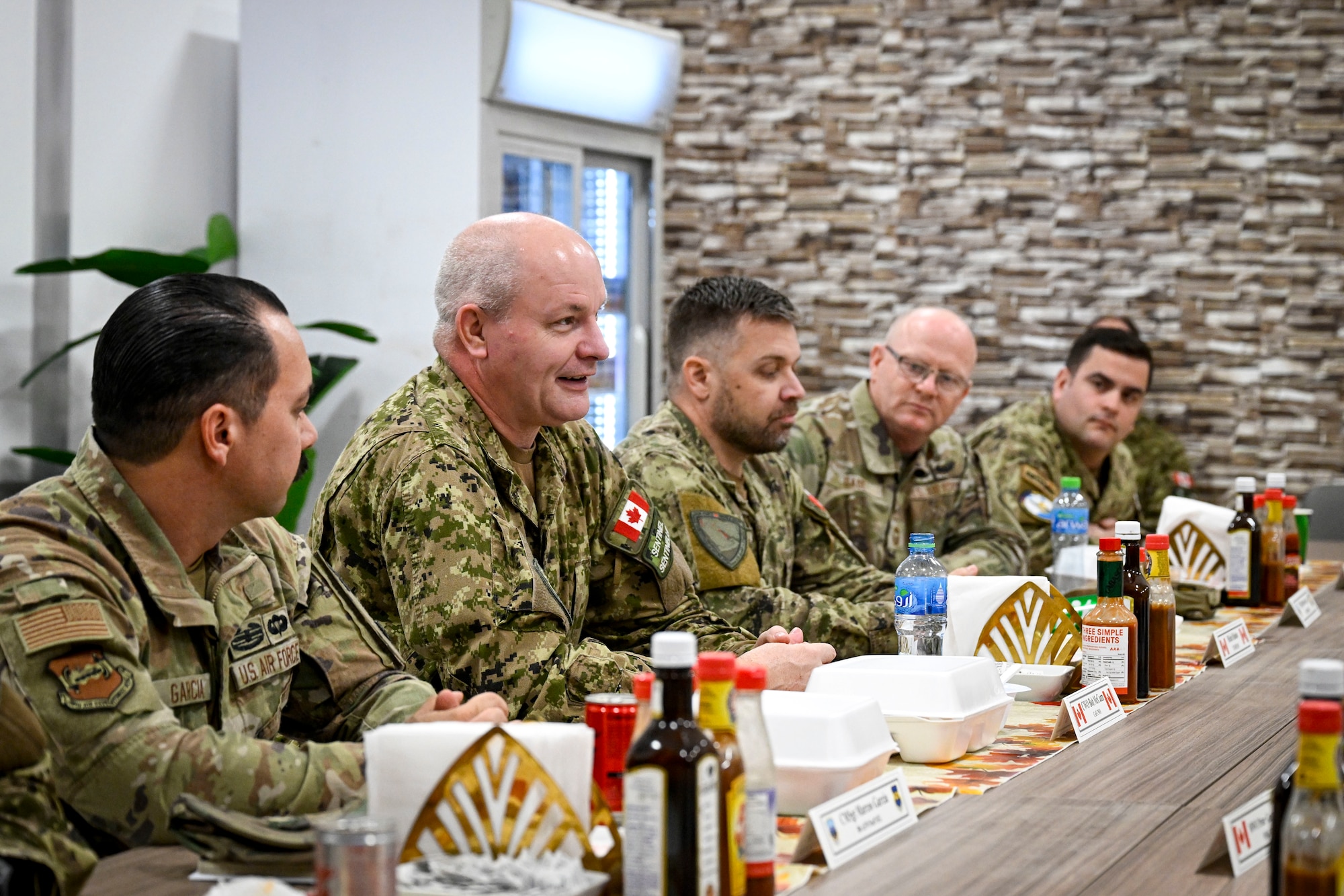 Canadian Armed Forces military members and U.S. Air Force military members talk while sitting at a table.