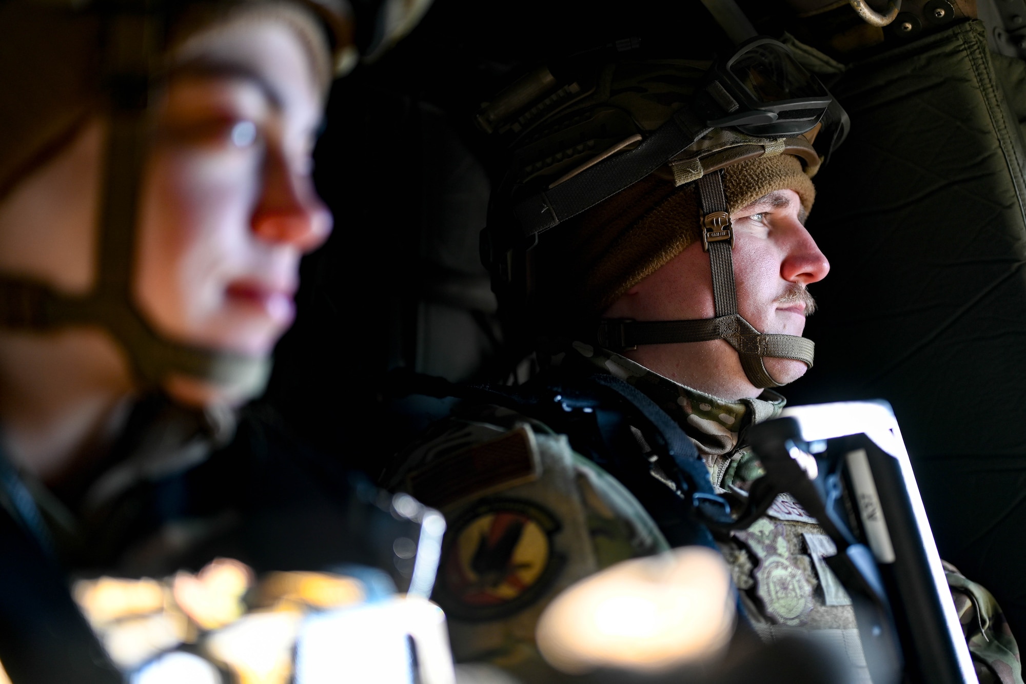 Two Airmen sit inside a helicopter.