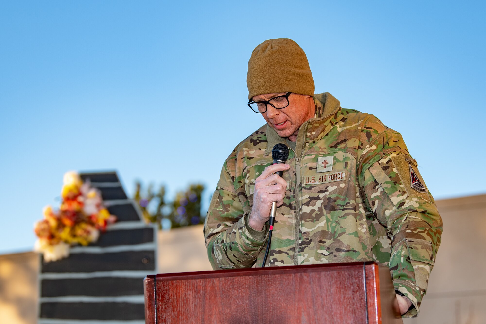 Maj. Kemp gives is standing behind a podium with his head bowed down as he gives a prayer.