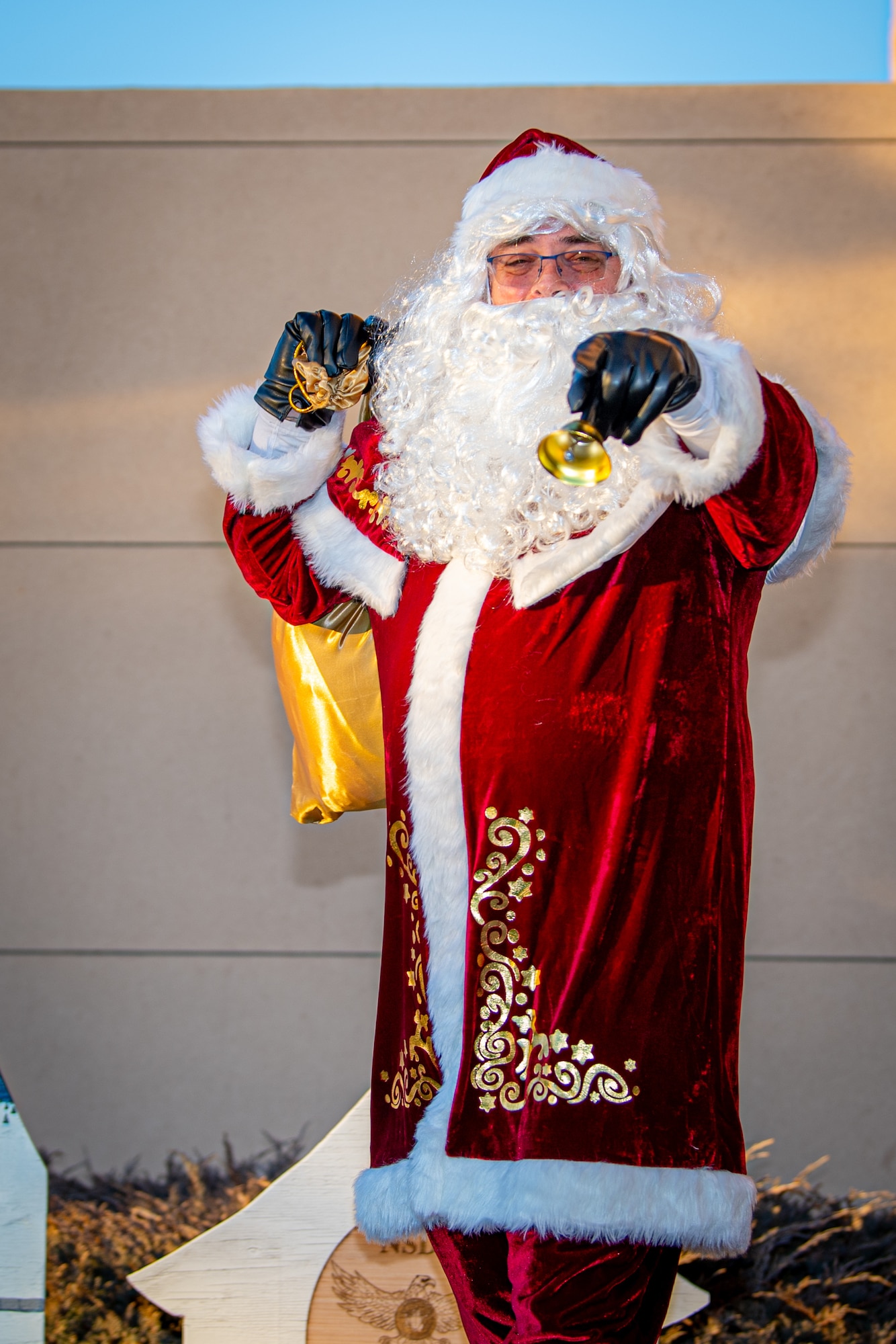 Santa Claus poses for a photograph while holding a little bell with his arm outstretched to the camera.