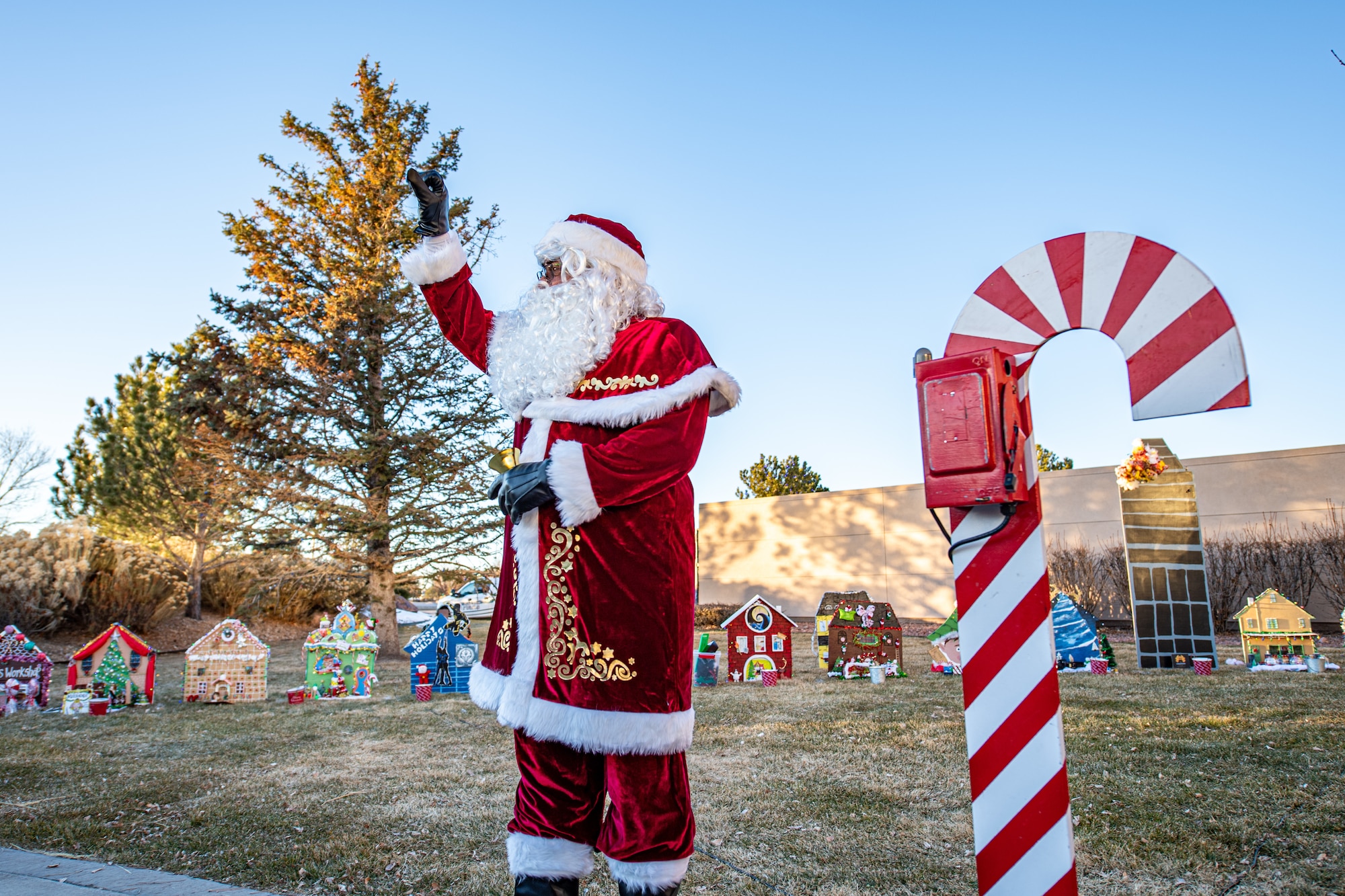 Santa Claus is waving while standing next to a candy cane decoration.