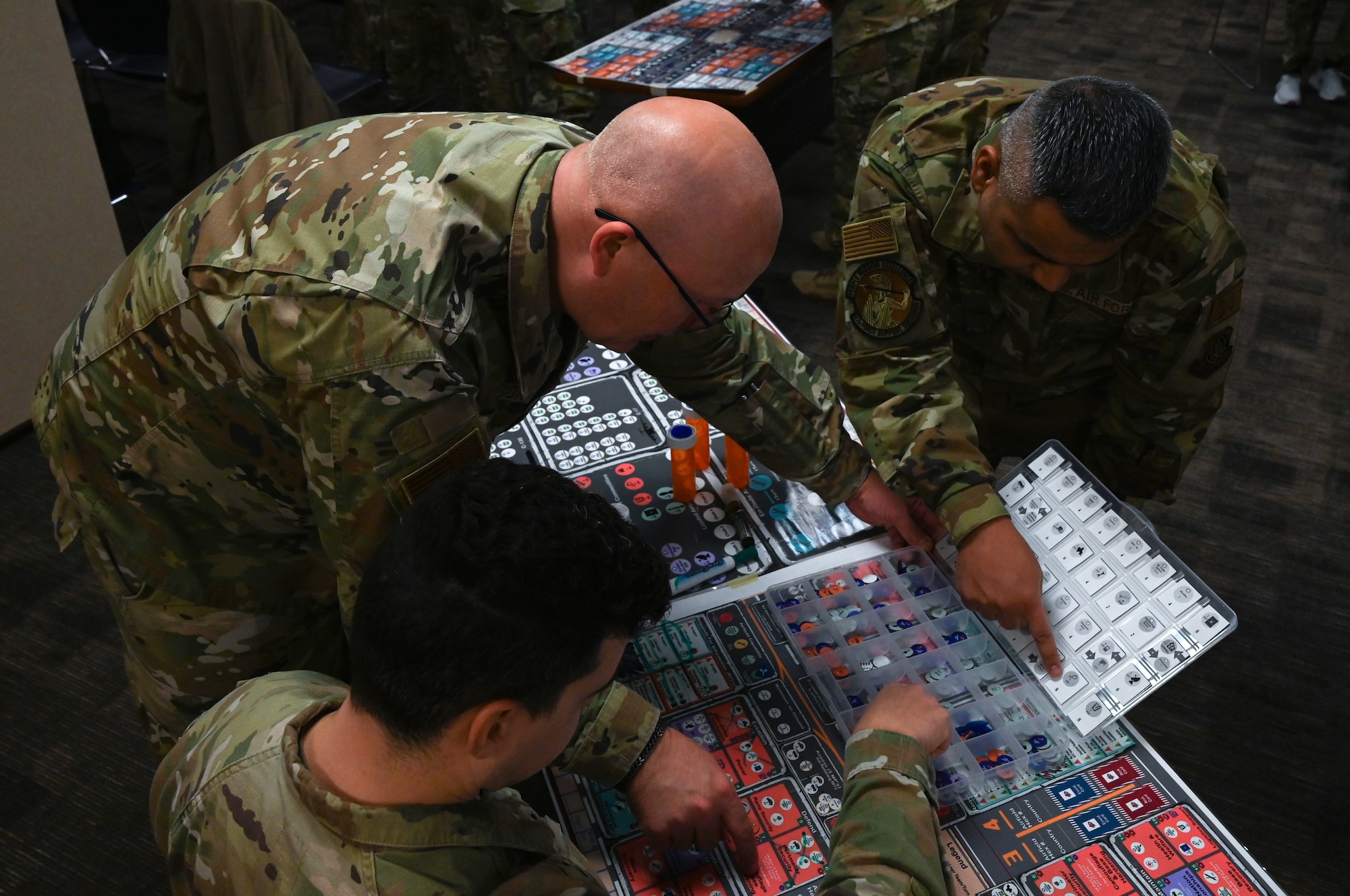 Several uniformed servicemembers huddle, roll dice and move small disks to advance a war board game called Kingfish ACE.