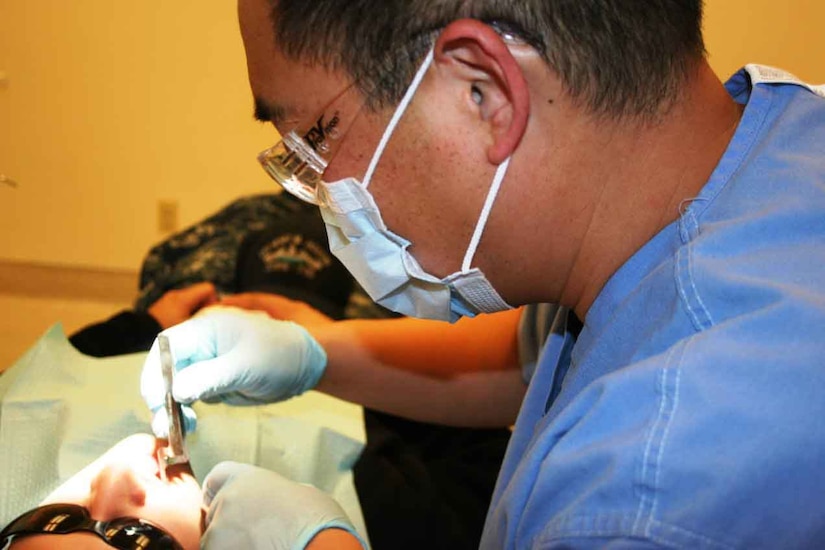 A dentist wearing gloves puts a tool into the mouth of a patient.