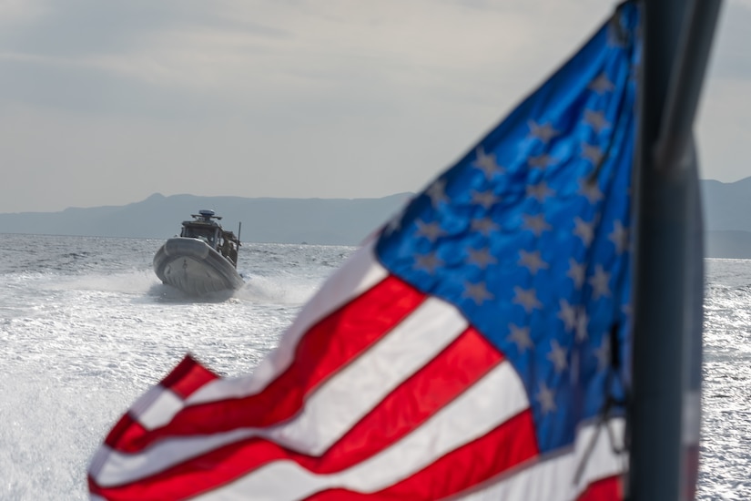 A boat operates in waters as an American flag waves in the foreground.