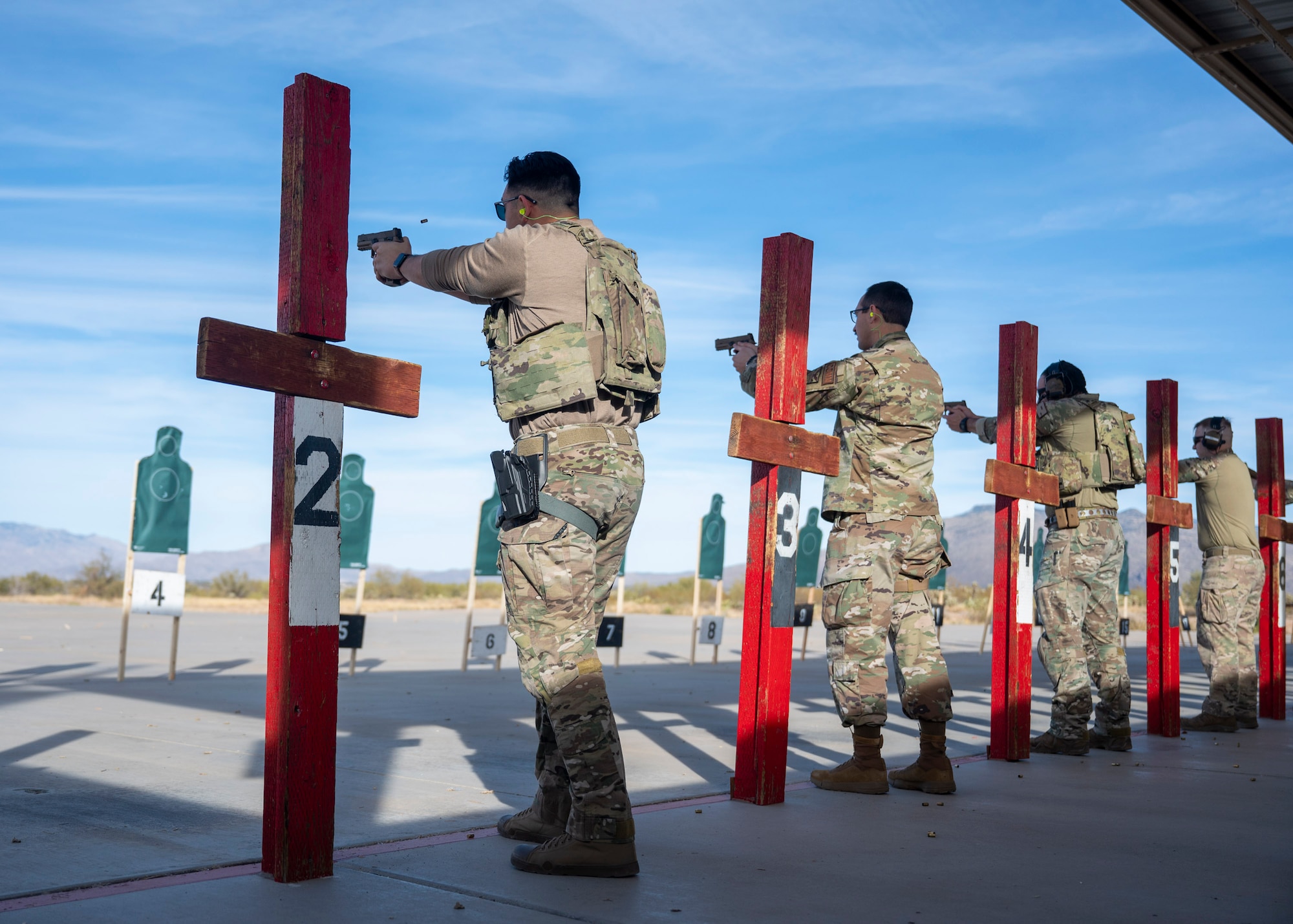 Men in military uniforms lineup and fire handguns at a firing range.