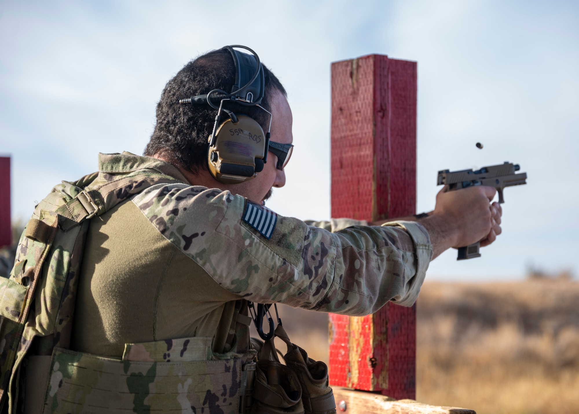 A man in a military uniform fires a Beretta M9 at a firing range.