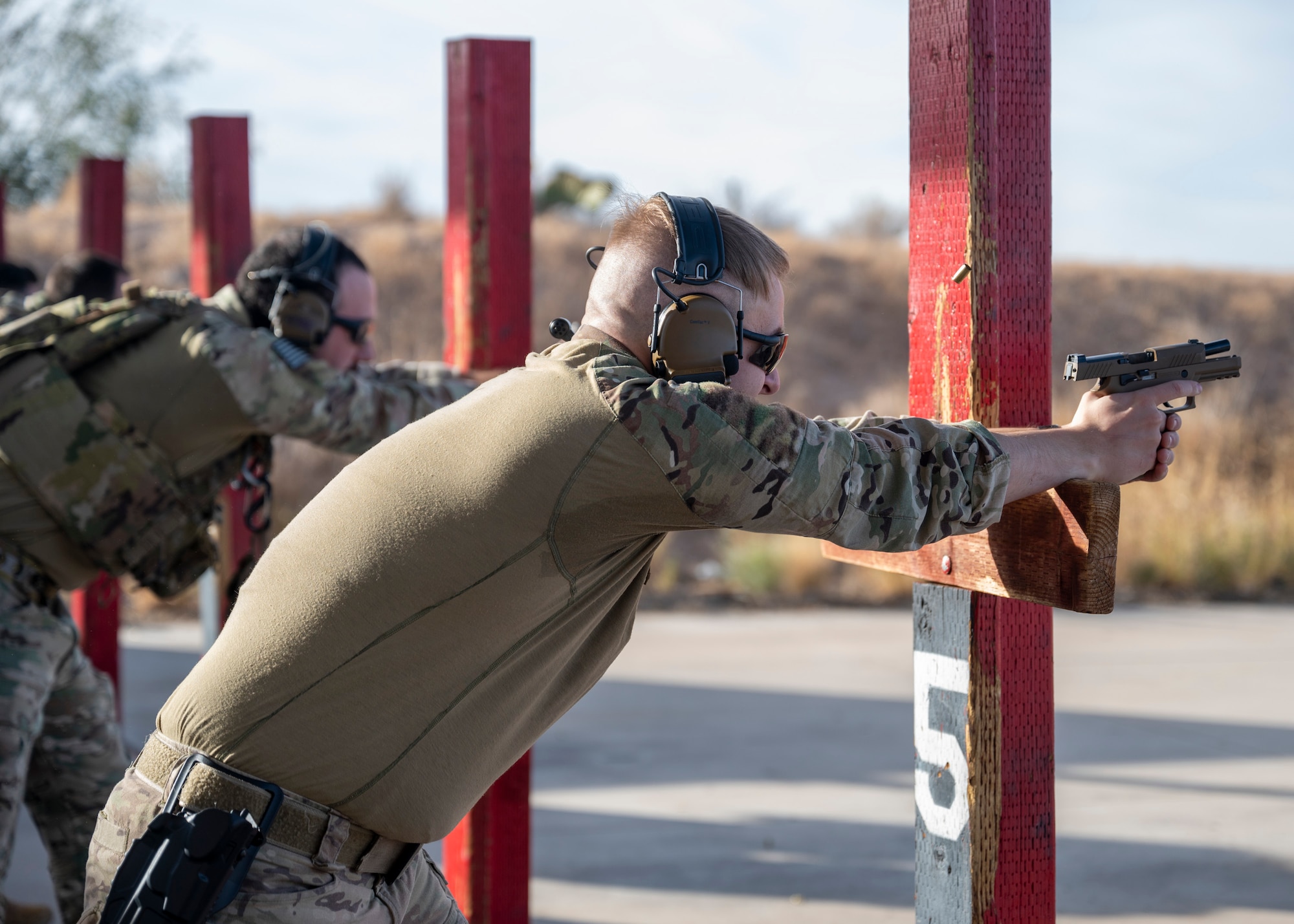 Men in military uniforms shoot Beretta M9 pistols in the leaning position at a firing range.