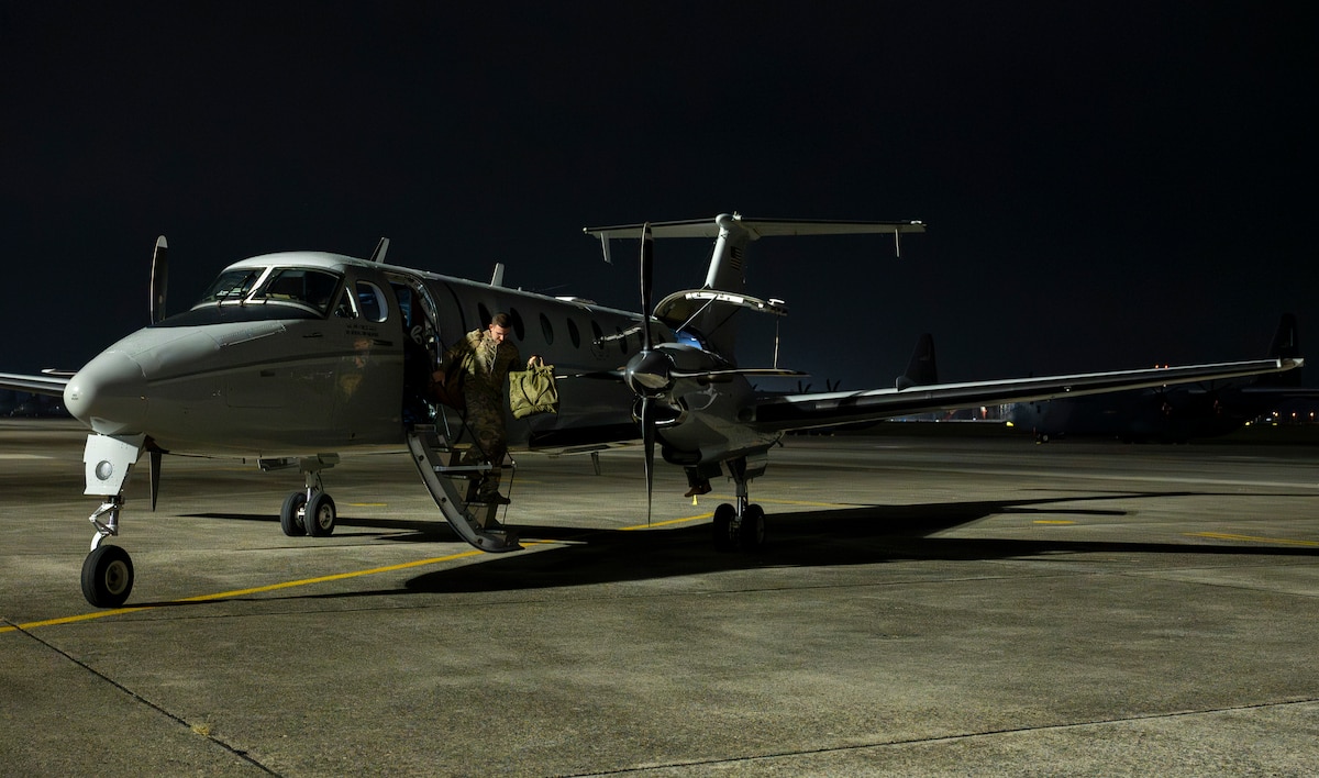 A military member walks down the steps of a C-12J Huron.