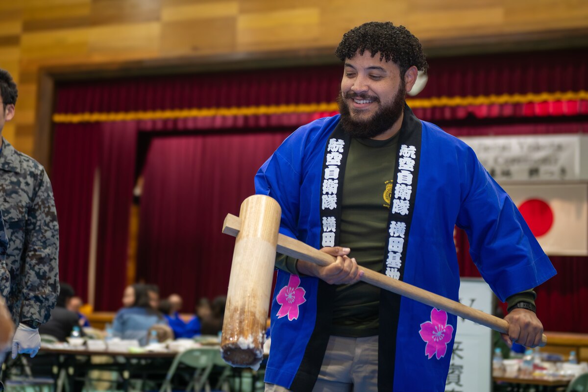 A mochi-pounding ceremony participant wears a blue Japanese traditional blouse while holding a wooden mallet.