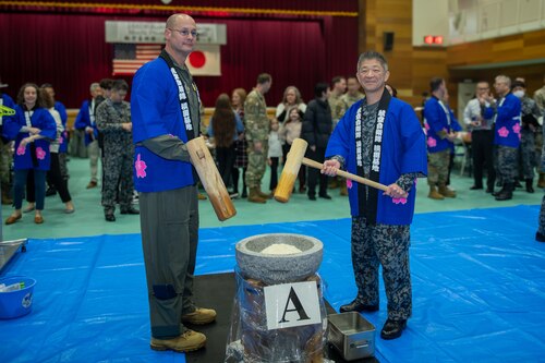Two people wearing blue blouses hold a wooden mallet as they pose for a photo.