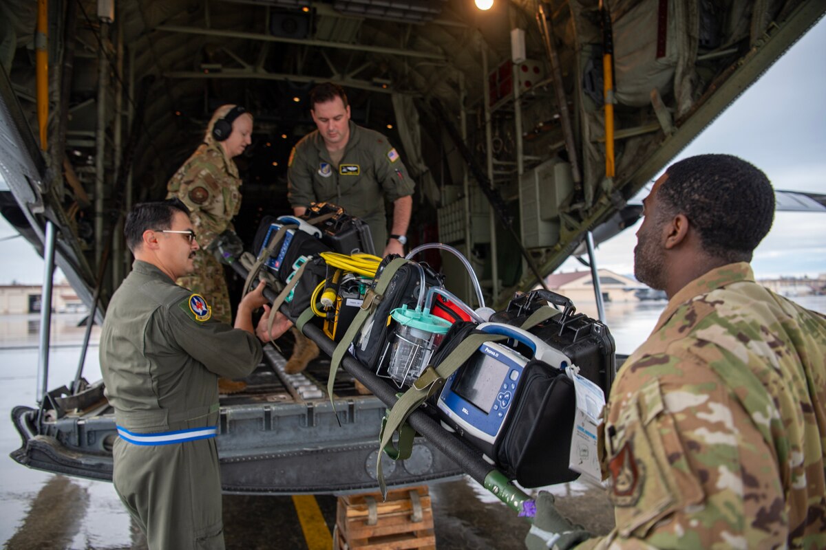 Four military members transfer medical equipment on to the back of a C-130J Super Hercules.