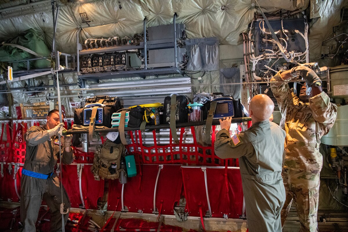 Three military members attach medical equipment onto a C-130J Super Hercules.