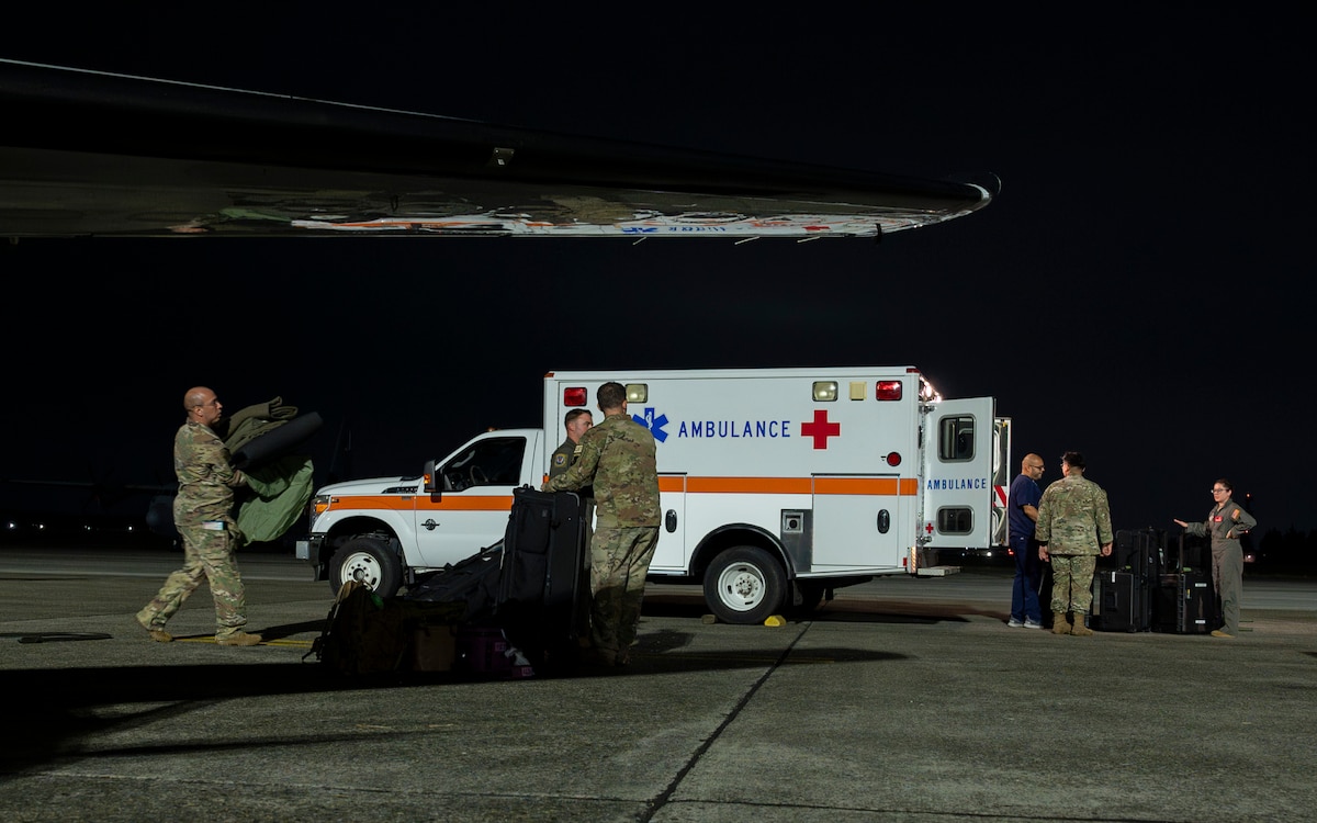 Military members carry medical equipment towards an ambulance.