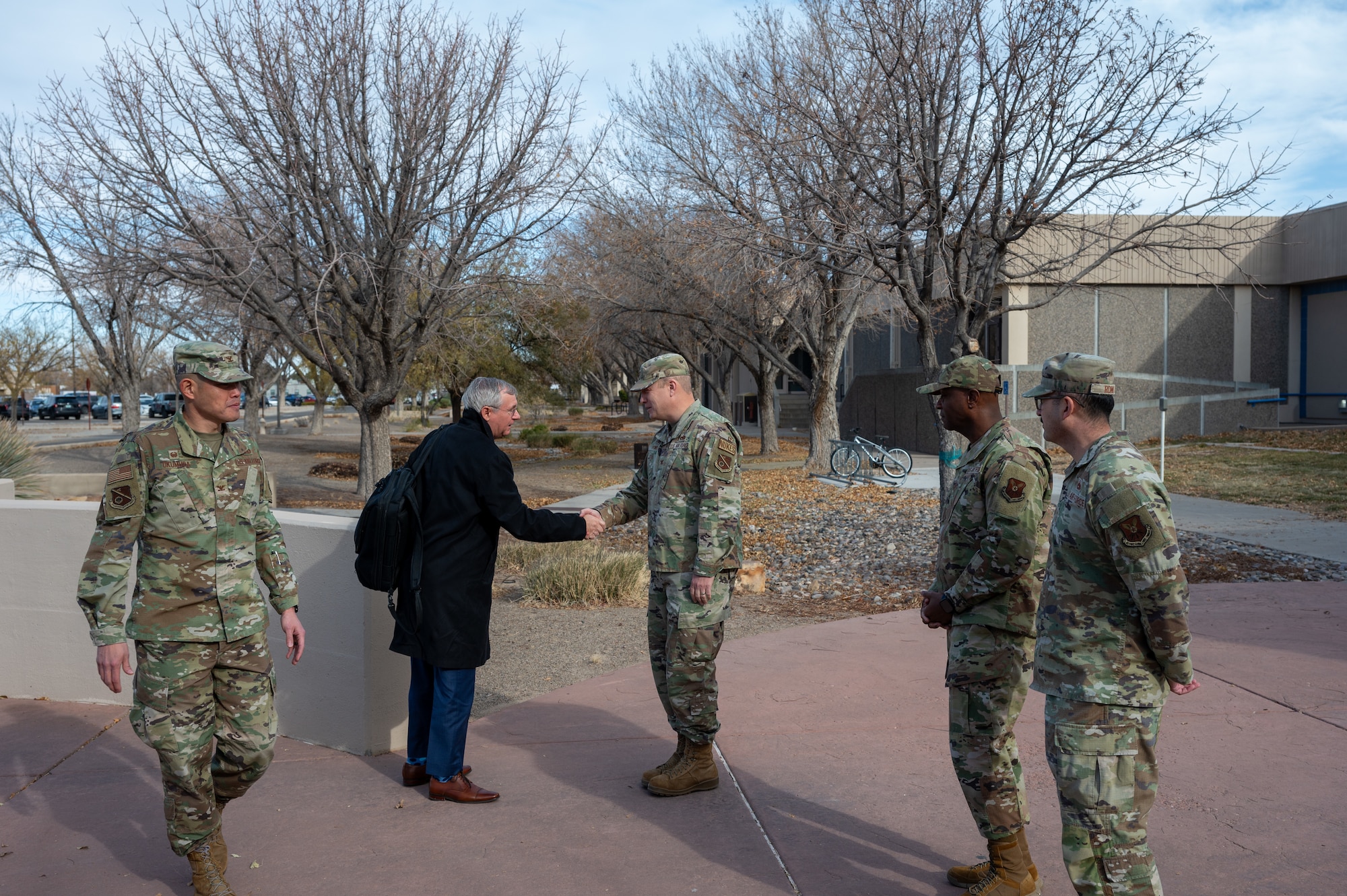 Military members shake hands with man in suit outside of buildling