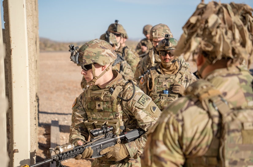 A group of soldiers prepare to enter a building in a deserted field.