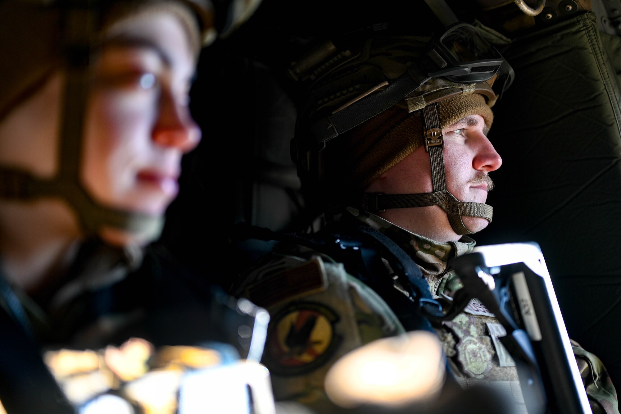 Two Airmen sit inside a helicopter.