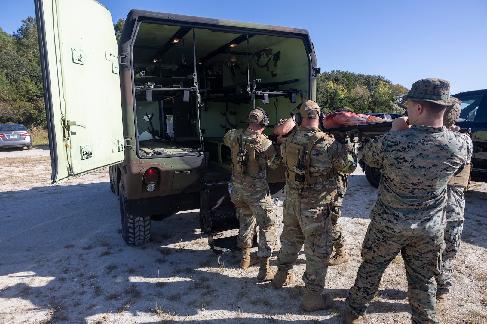 Military members lift a simulated casualty on a stretcher to load into the back of a medical transport vehicle.