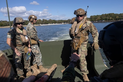 Three military members riding on a boat transporting a simulated casualty.