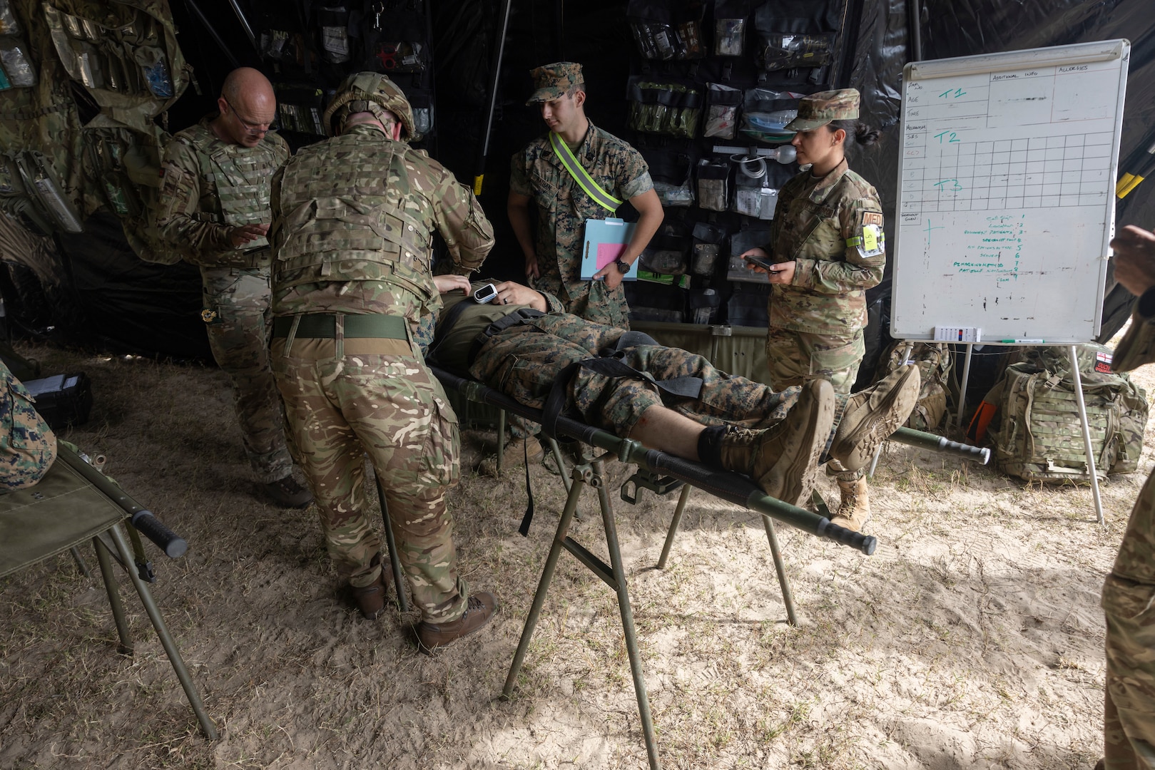 Four military members assessing simulated casualty on a stretcher.