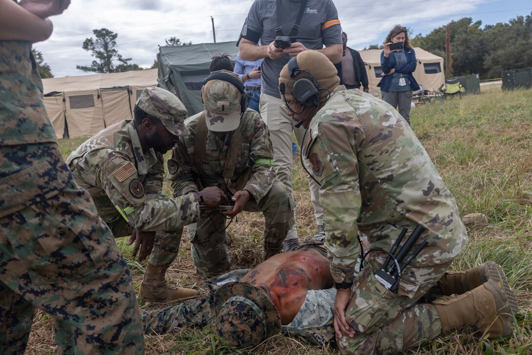 Three military members assess a simulated casualty lying on the ground.