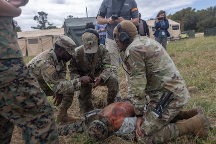 Three military members assess a simulated casualty lying on the ground.