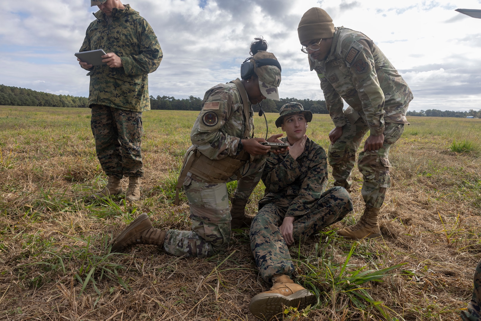 Two military members assess a simulated casualty sitting on the ground.