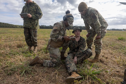 Two military members assess a simulated casualty sitting on the ground.