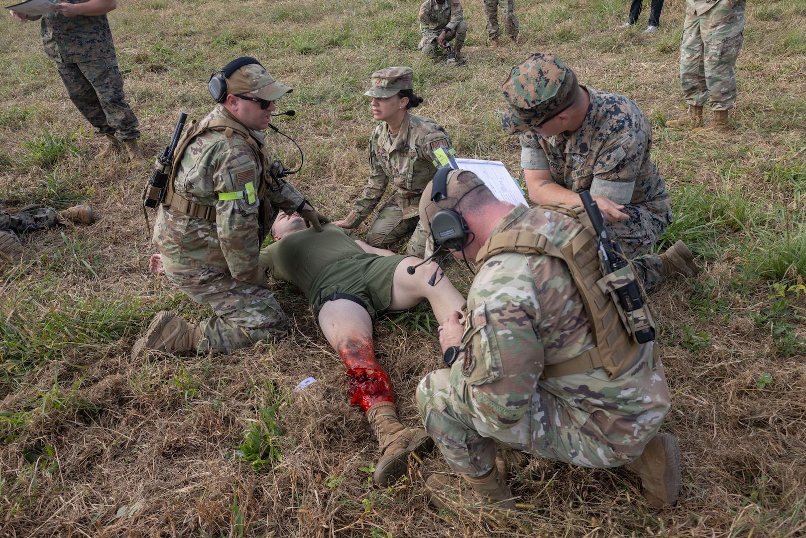 Four military members assess a simulated casualty lying on the ground.