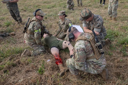 Four military members assess a simulated casualty lying on the ground.