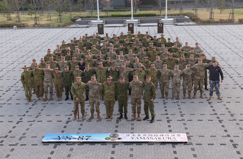 More than 100 multinational service members stand for a photo on a hardscaped surface outdoors.