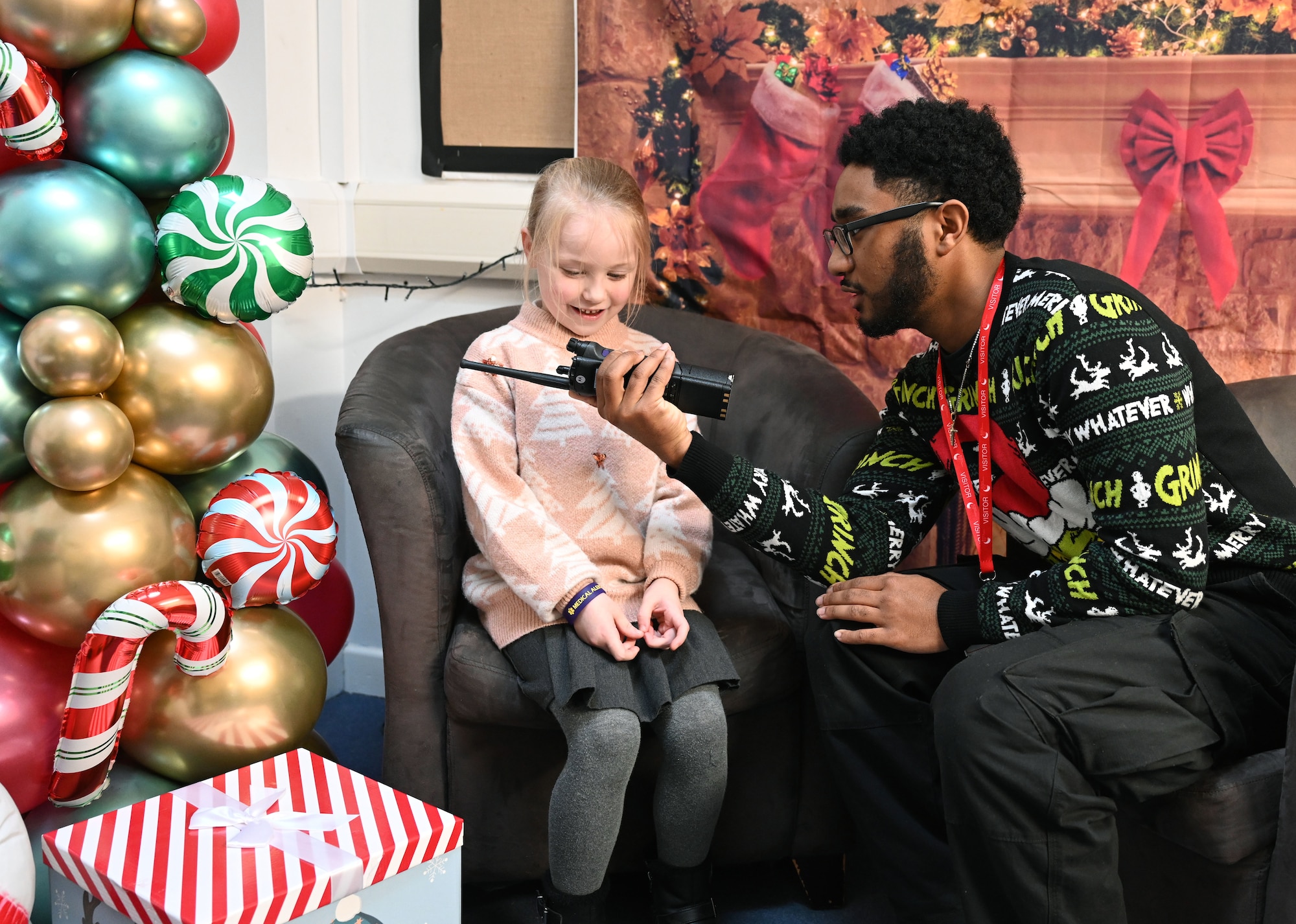 U.S. Air Force Airman 1st Class Jeffrey Favor, 100th Communications Squadron radiofrequency transmissions technician, uses a hand-held radio to encourage a Year-1 child to interact with Santa at Beck Row Primary Academy, Beck Row, England, Dec. 12, 2024. A team of eight Airmen and civilians from Royal Air Force Mildenhall spent time with 81 children and provided them a chance to talk to Santa and make special gift requests before the holidays. (U.S. Air Force photo by Karen Abeyasekere)