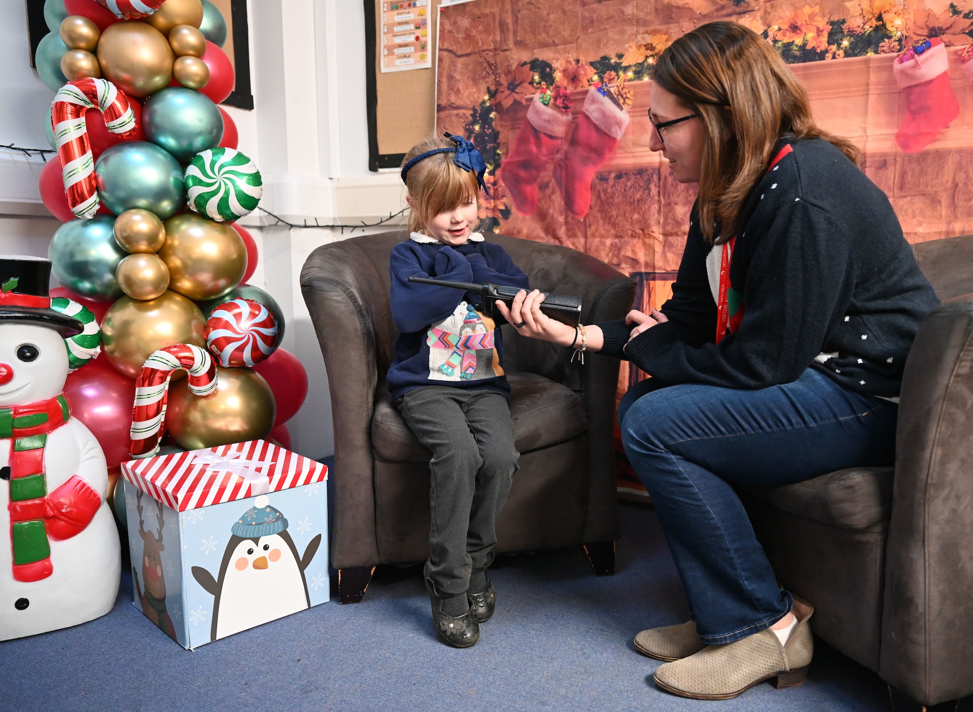U.S. Air Force Senior Airman Sharon Bremar, 100th Communications Squadron agile combat employment technician, uses a hand-held radio to encourage a Reception-Year child to interact with Santa at Beck Row Primary Academy, Beck Row, England, Dec. 12, 2024. A team of eight Airmen and civilians from Royal Air Force Mildenhall visited the primary academy and provided 81 children a chance to talk to Santa and make special gift requests before the holidays. (U.S. Air Force photo by Karen Abeyasekere)