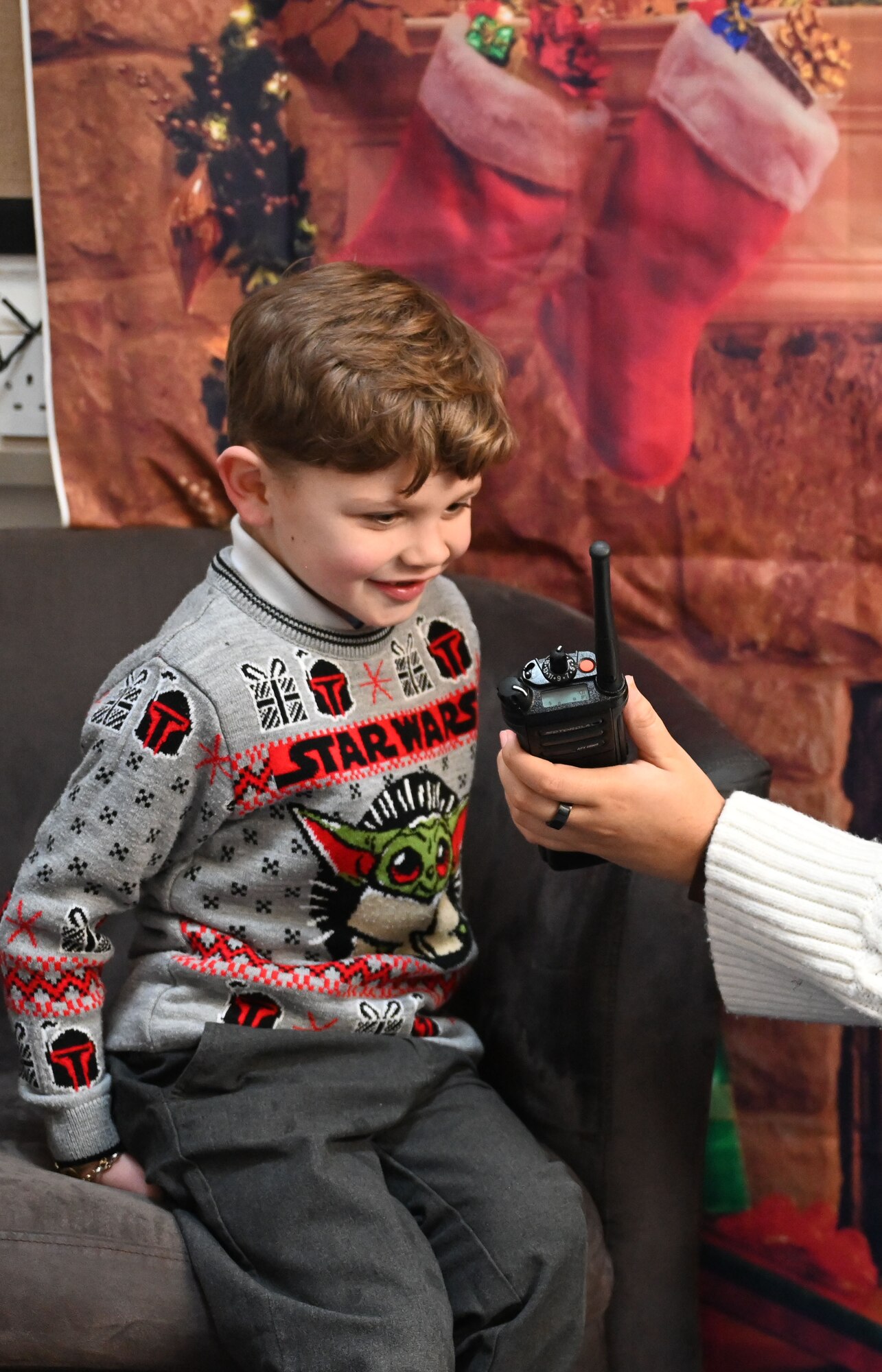 A Reception-Year student speaks to Santa via a hand-held radio, helped by a U.S. Air Force Airman from the 100th Communications Squadron, at Beck Row Primary Academy, Beck Row, England, Dec. 12, 2024. A team of eight Airmen and civilians from Royal Air Force Mildenhall spent time with 81 children and provided them a chance to talk to Santa and make special gift requests before the holidays. (U.S. Air Force photo by Karen Abeyasekere)