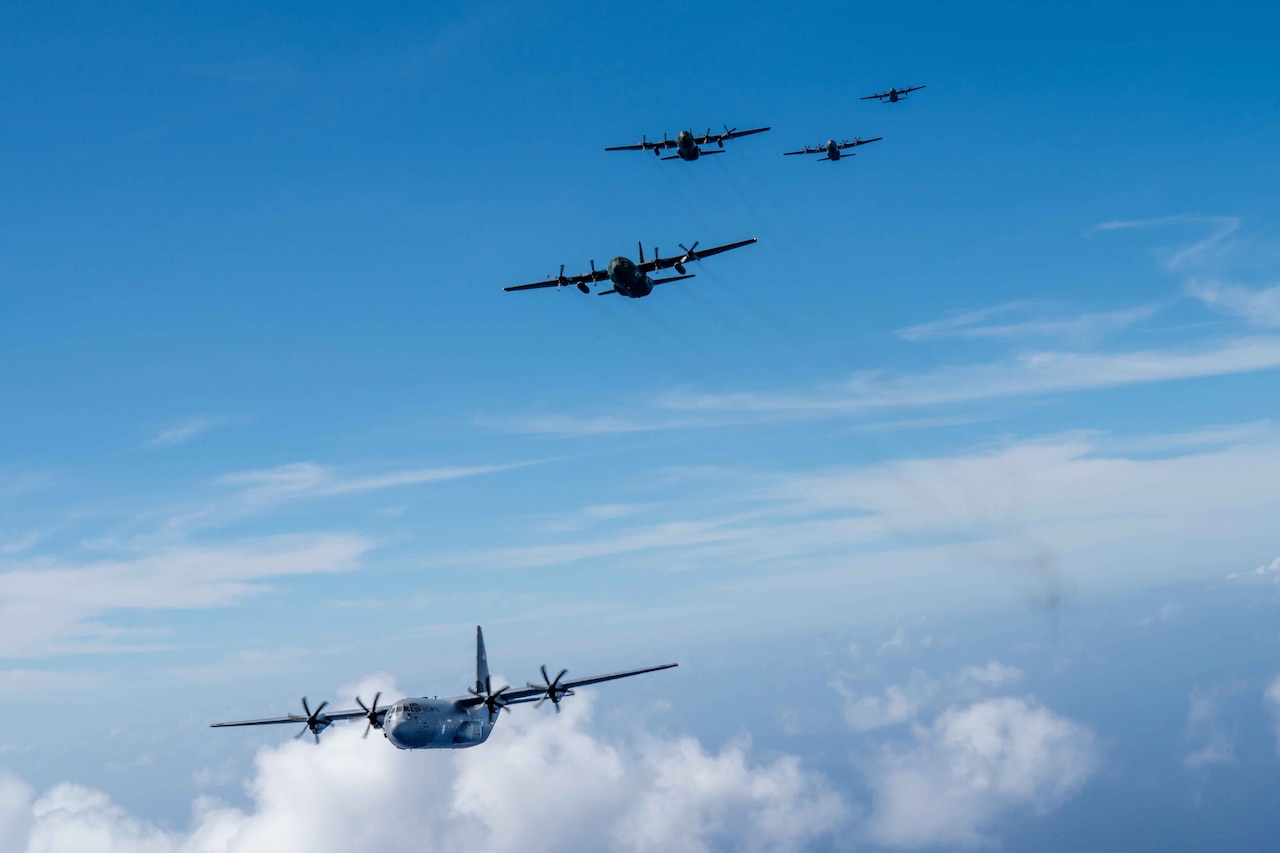 Five large military aircraft fly together on a sunny day.