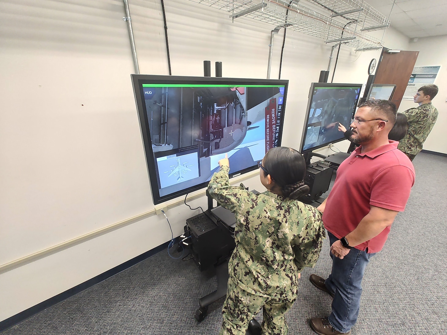 Under the supervision of Center for Naval Aviation Technical Training Instructor Coy Weese (right), Aviation Machinist’s Mate Airman Jhianna Baker (left) practices conducting maintenance on the E-6B Mercury using the new Multi-Purpose Reconfigurable Training System 3D Panel Trainers at Tinker Air Force Base, Oklahoma.