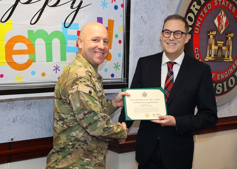 A man in an Army uniform presents a certificate to a man wearing a suit.
