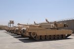 M1A1 tanks lined up on cement inside a desert base